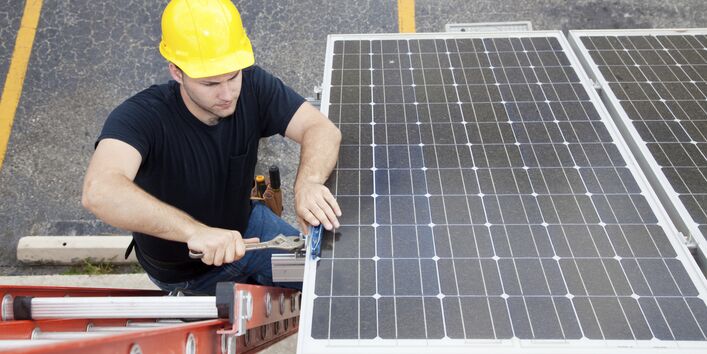 Ein Mann mit Bauhelm auf einer Leiter montiert eine Photovoltaikanlage