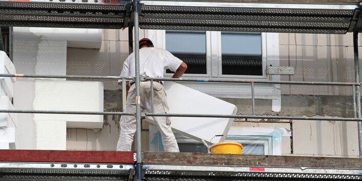 Bauarbeiter auf einem Gerüst bringen Dämmplatten an der Fassade eines Mehrfamilienhauses an.