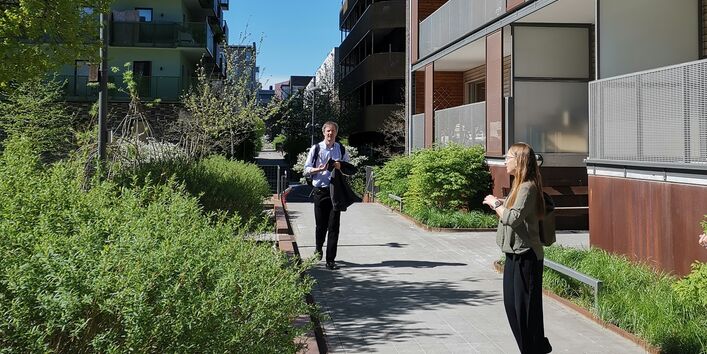 Menschen auf einem Fußweg in einer begrünten mehrgeschossigen Wohnsiedlung mit Balkonen