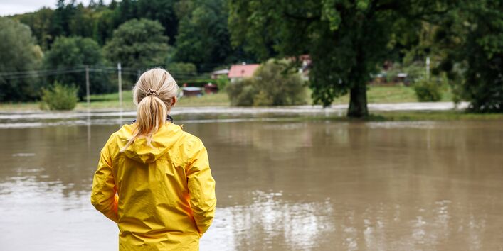 Eine Frau in einer gelben Regenjacke betrachtet eine überflutete Straße.