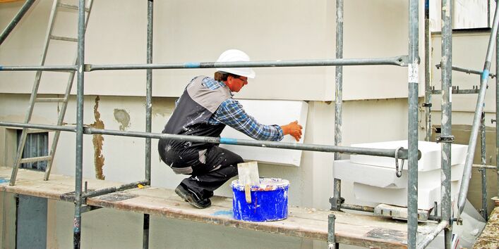 Eine Bauarbeiter bringt Dämmplatten an einem Gebäude an.