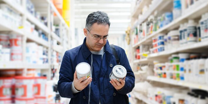 Ein Kunde betrachtet im Geschäft eingehend zwei Dosen mit Lack, die er in der Hand hält