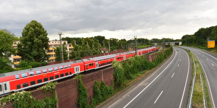 Fahrender Zug neben Bundesstraße nahe einem Wohngebiet