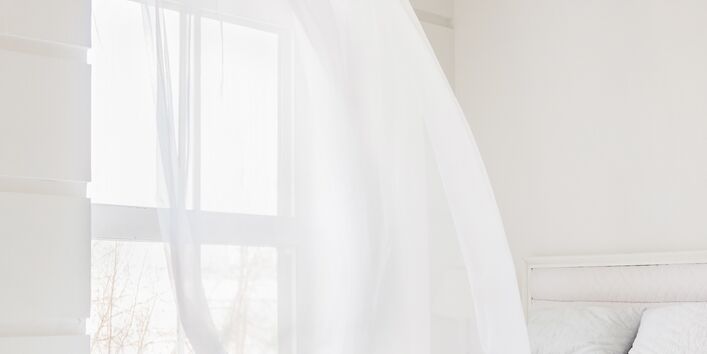 Lüften eines Schlafzimmers: der Vorhang weht über das Bett.