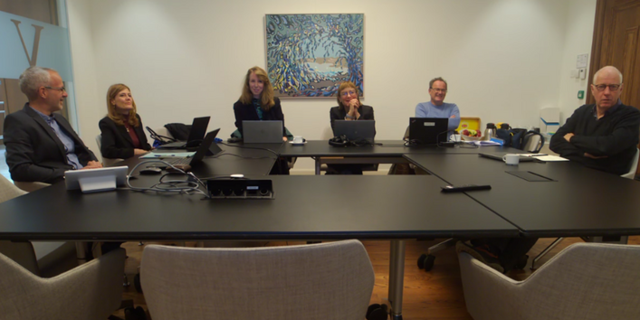 In a small meeting room, 7 people sit at a table.