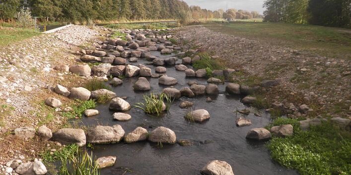 Foto: Die fertiggestellte Fischaufstiegsanlage in Lüssow. Eine langgezogene Gleite mit vielen größeren Steinblöcke im Gewässer ersetzt das alte Streichwehr.