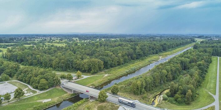 Luftbild des Flusses Murg bei Rastatt. Entlang des geradlinigen Hauptgerinnes liegt ein strukturreiches Nebengerinne, das als Überflütungsfläche für Hochwasser dient. Im Hintergrund liegen ausgedehnte Auwaldflächen. Am Bildrand stehen Gebäude der Stadt.