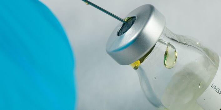 Foto einer Arzneimittelflasche an der eine Spritze aufgezogen wird.