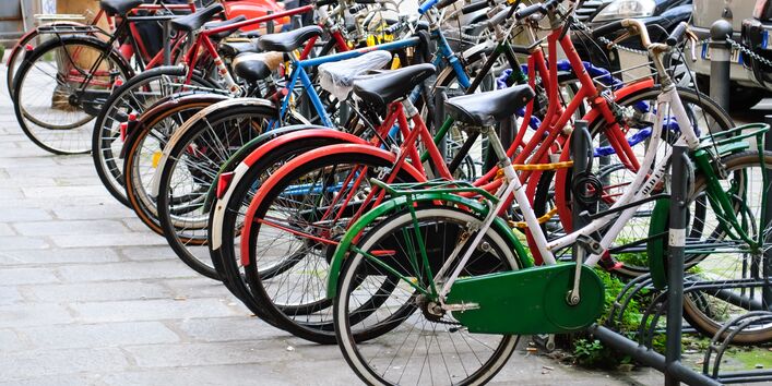 an einem Fahrradständer parken viele Fahrräder gegenüber von vielen geparkten Autos