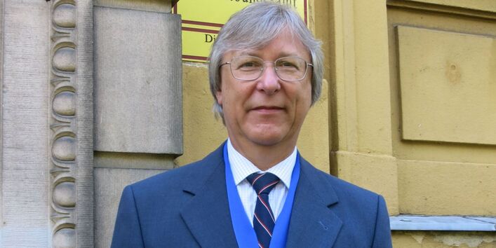 ein Mann in Anzug und Krawatte und mit einer Medaille um den Hals vor einem Gebäude mit einem Schild mit der Aufschrift "Umweltbundesamt"