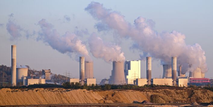 rauchende Schornsteine eines Braunkohlekraftwerks, davor ein Tagebau