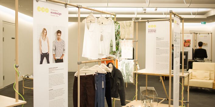 Ausstellung mit Plakaten, die an Holzstangen angebracht sind, und Exponaten wie Kleidung und Schuhen