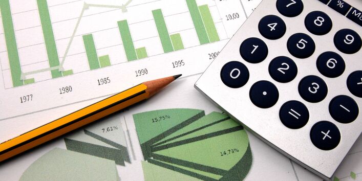 Taschenrechner, Bleistift und Zettel mit grünen Säulen- und Tortendiagrammen
