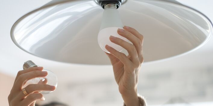 eine Frau tauscht eine Glühbirne gegen eine LED-Lampe aus