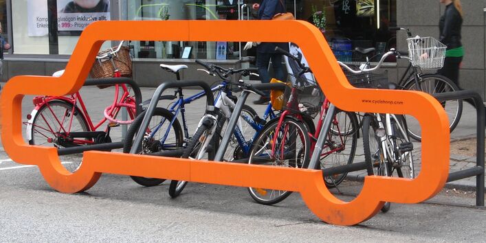 an der Front eines Fahrradständers für mehrere Räder in der Stadt ist ein lebensgroßer Umriss eines Autos angebracht und verdeutlicht: wo sonst nur ein Auto hinpasst, passen viele Fahrräder hin