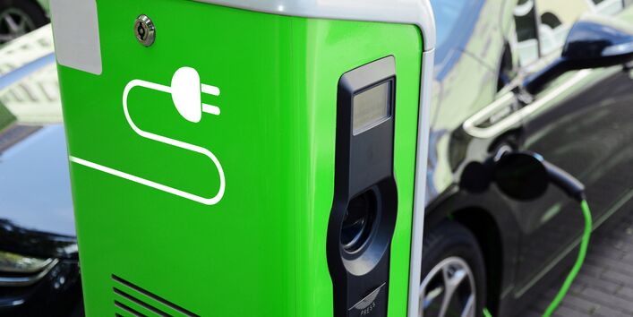 ein Elektroauto tankt Strom an einer grünen Ladesäule