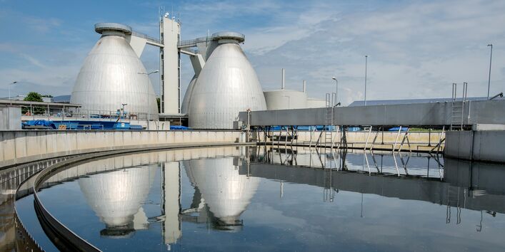 zwei Faultürme einer Kläranlage spiegeln sich in einem Nachklärbecken.