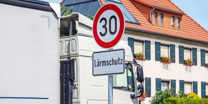 Ein Lkw fährt durch ein Wohngebiet, an der Straße steht ein Verkehrsschild "Tempo 30 Lärmschutz".