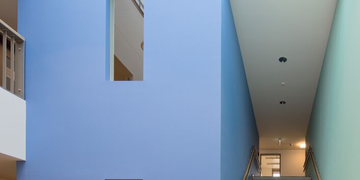 kleine Eingangshalle mit Glasdach und Treppenaufstieg, die Wände sind weiß, die Wände des Treppenhauses jedoch links blau uns rechts hellgrün gestrichen