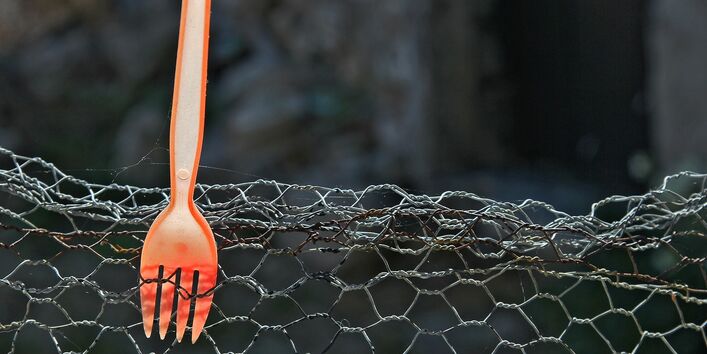 auf einem Maschendrahtzaun spießt eine orange Plastikgabel