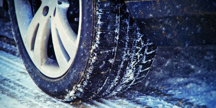 ein Auto fährt bei Schneetreiben über eine verschneite Fahrbahn, Großaufnahme eines Reifens