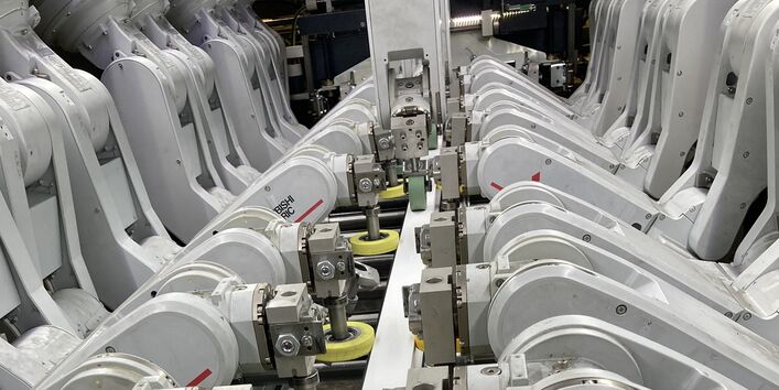 technische Anlage mit 12 Roboterarmen, die eine Folie auf ein PVC-Profil aufbringen