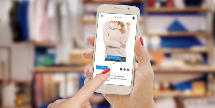 eine Frau bestellt vor ihrem Kleiderschrank mit ihrem Smartphone Kleidung