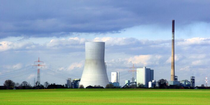 Kraftwerk mit einem Schlot und einem Kühlturm, daneben ist eine Energiefreileitung zu sehen