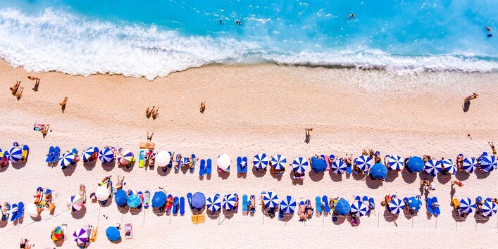 Menschen an einem Meeresstrand mit Sonnenschirmen von oben
