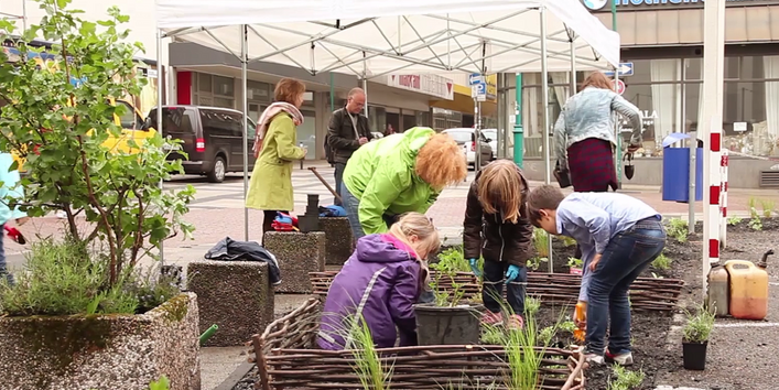 Kinder und Erwachsene bepflanzen Hochbeete und Blumenkübel in der Stadt