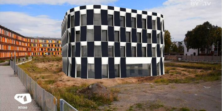 neben dem UBA-Gebäude Dessau-Roßlau ist eine Brache mit Bauzaun. Per Computersimulation wurde der geplante Erweiterungsbau mit seinen großen Photovoltaikelementen an der Fassade, reingesetzt.