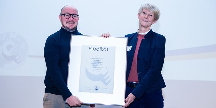 eine Frau und ein Mann posieren mit einer Urkunde für ein Foto