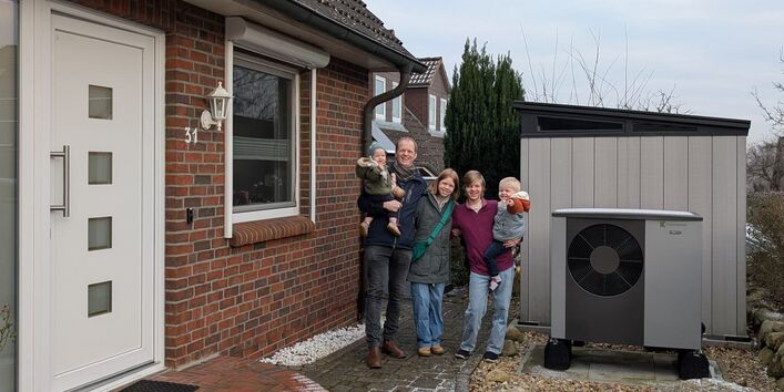 Familie vor einem Einfamilienhaus mit Wärmepumpe