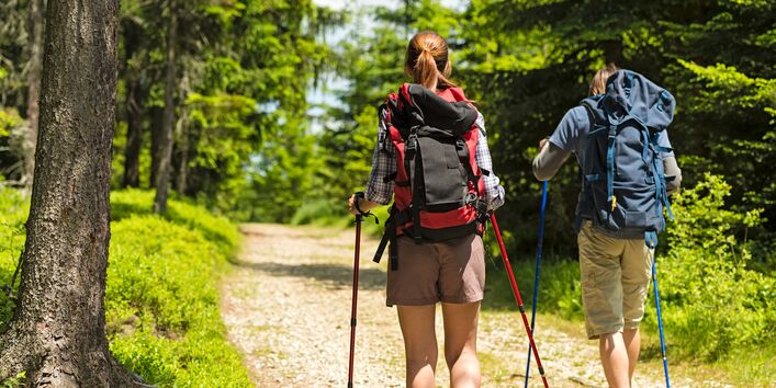 eine Frau und ein Mann beim Wandern mit Wanderrucksäcken und Wanderstöcken auf einem Waldweg