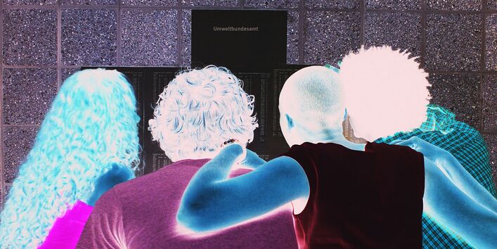 Vier junge Menschen beugen sich über eine Pinnwand mit Aushängen