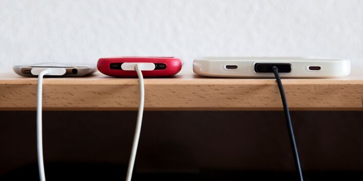 Drei Smartphones werden gleichzeitig über ihre Ladegeräte mit Strom geladen. 