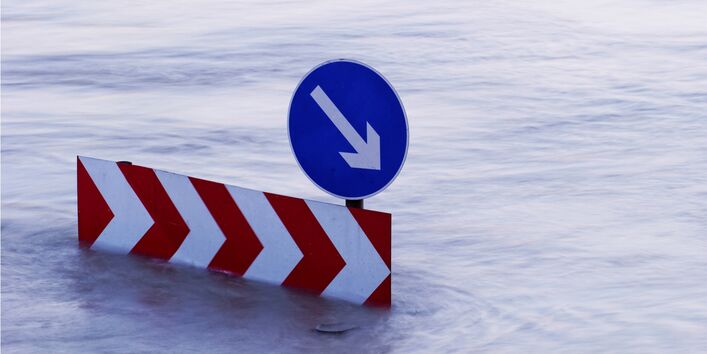 Ein Verkehsschild steht mitten im Hochwasser. Die Straße ist nicht mehr zu sehen.