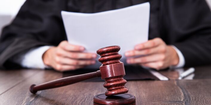 Ein Richter mit Hammer und Verhandlungsunterlagen sitzt an einem Tisch.