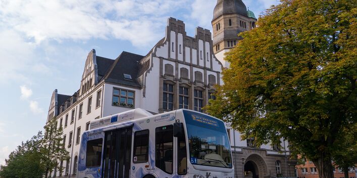 Ein mit Wasserstoff betriebener Kleinbus steht auf der Straße vor einem alten Gebäude und einem Baum