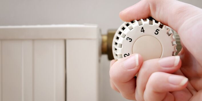 Nahaufnahme: Eine Hand dreht das Thermostat einer Heizung auf.