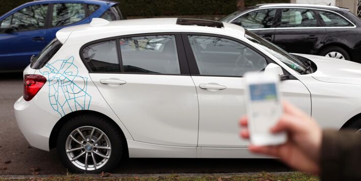 Carsharingauto, im Vordergrund Mann mit Handy