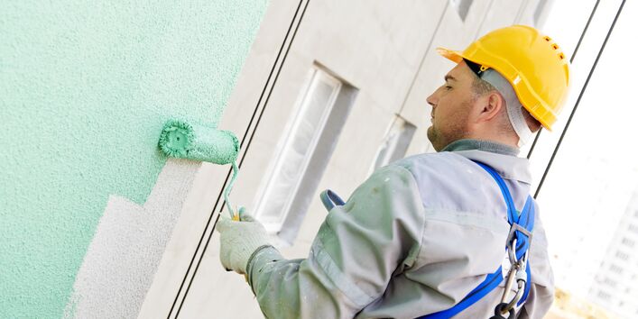 Arbeiter streicht Hausfassade grün an