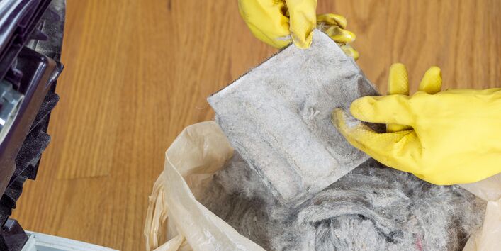 geöffneter Staubsauger, Staubbeutel ist in der Mülltüte und eine Person zeigt den Staubfilter