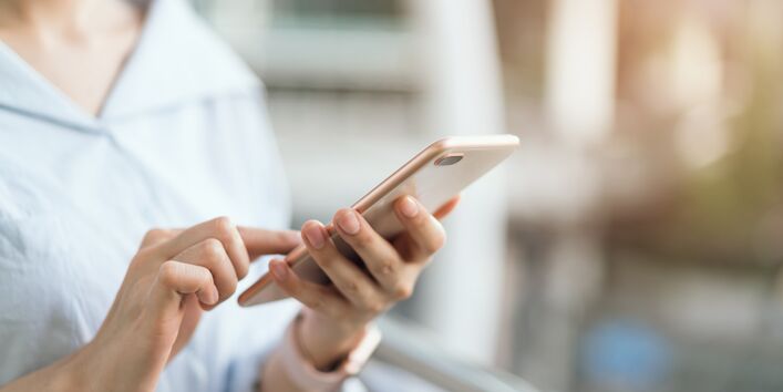 Eine Frau hält ein Smartphone in der Hand und tippt mit der anderen Hand darauf