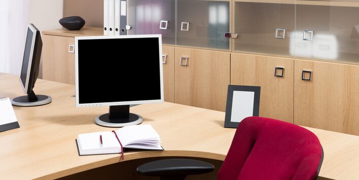 ein Schreibtisch mit Computer, dahinter Büroschränke