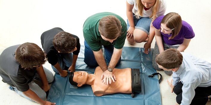 Jugendliche üben Herzmassage am Torso einer Übungspuppe im Erste Hilfe Kurs .