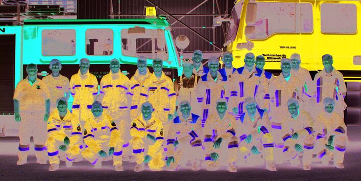 Einsatzkräfte in Uniformen des THW und einer Feuerwehr als Gruppenfoto vor ihren Einsatzfahrzeugen.