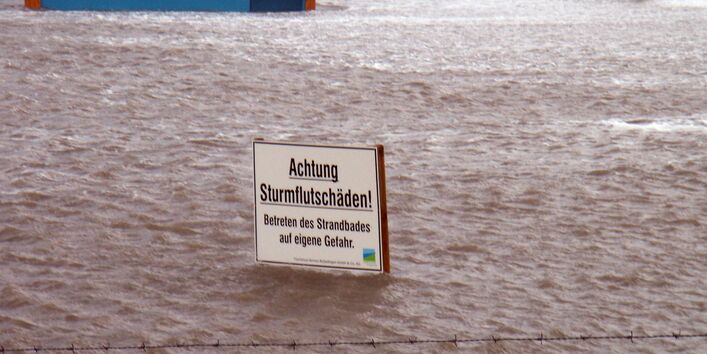 Warnschild vor Sturmflutschäden in überfluteter Hafenanlage.