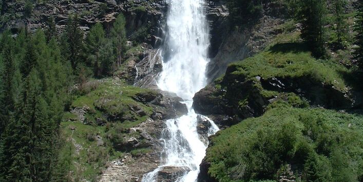 Ein langer Wasserfall mit Tannen und Gebüsch rechts und links
