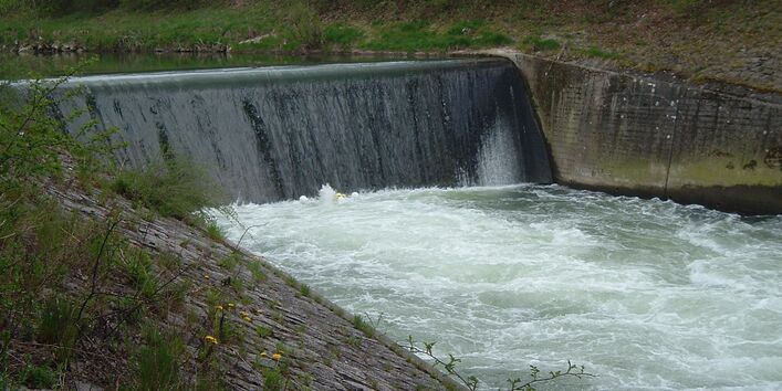 Querbauwerk in einem Fluss - Wasser fließt senkrecht eine Wand herunter